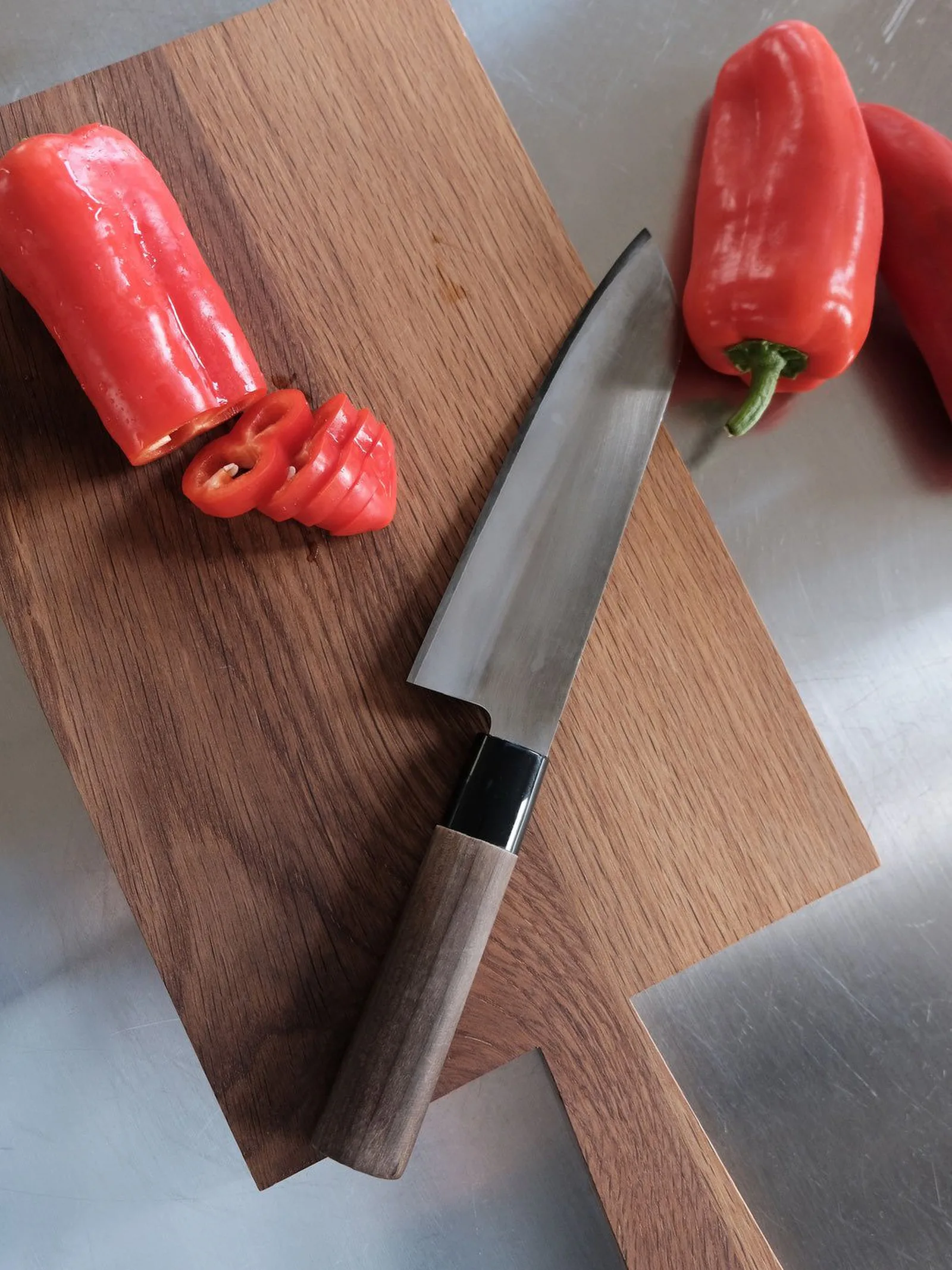 Ein frisch geschliffenes Küchenmesser auf einem Holzbrett neben aufgeschnittenen roten Peperoni