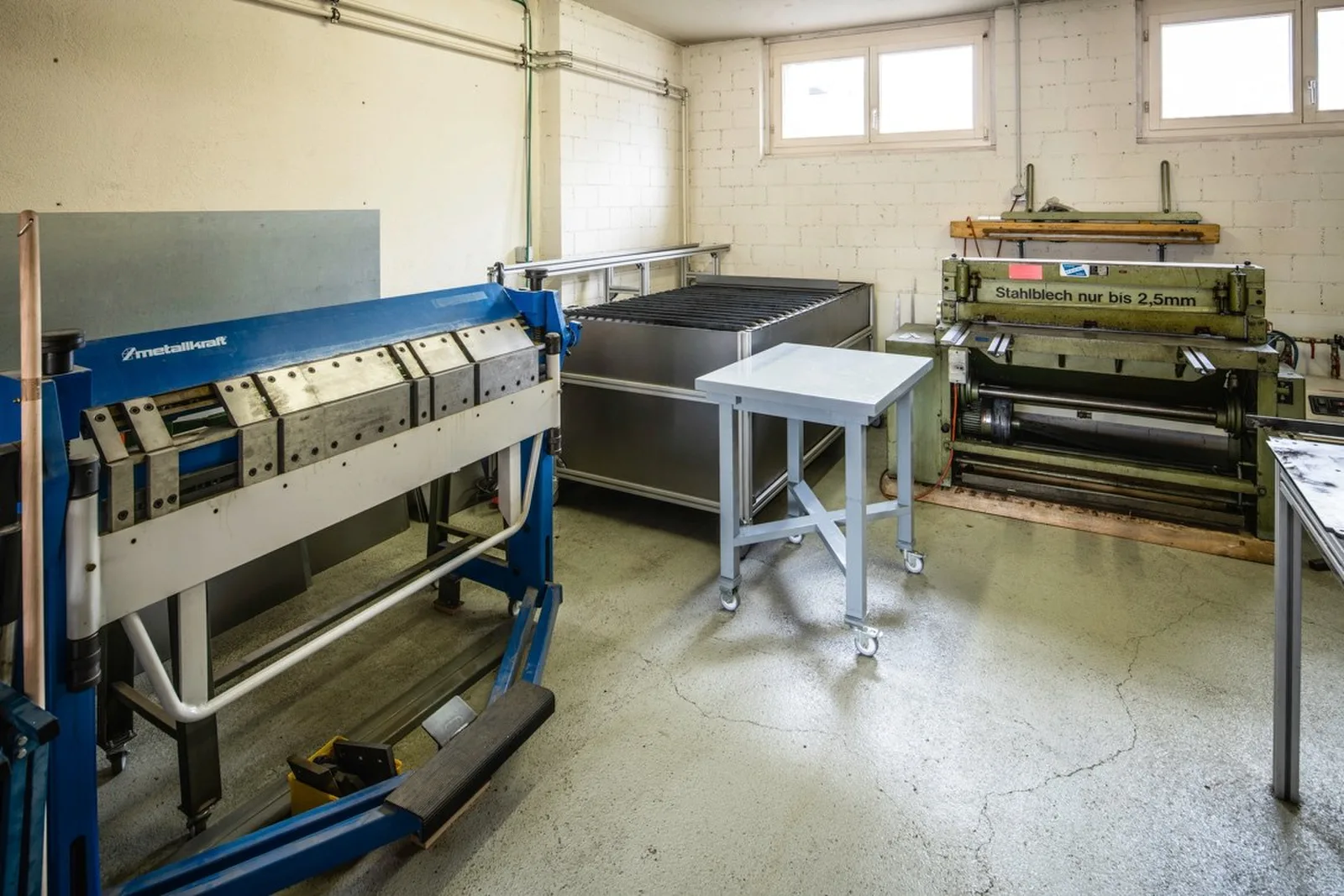 Blaue Abkantbank und Schlagschere im Metallraum der Buitig, dazwischen ein Stahltisch auf Rollen