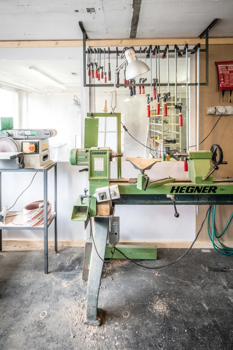 Grüne Drechselbank im Holzraum der Buitig, dahinter eine Wand mit aufgereihtem Drechselwerkzeug