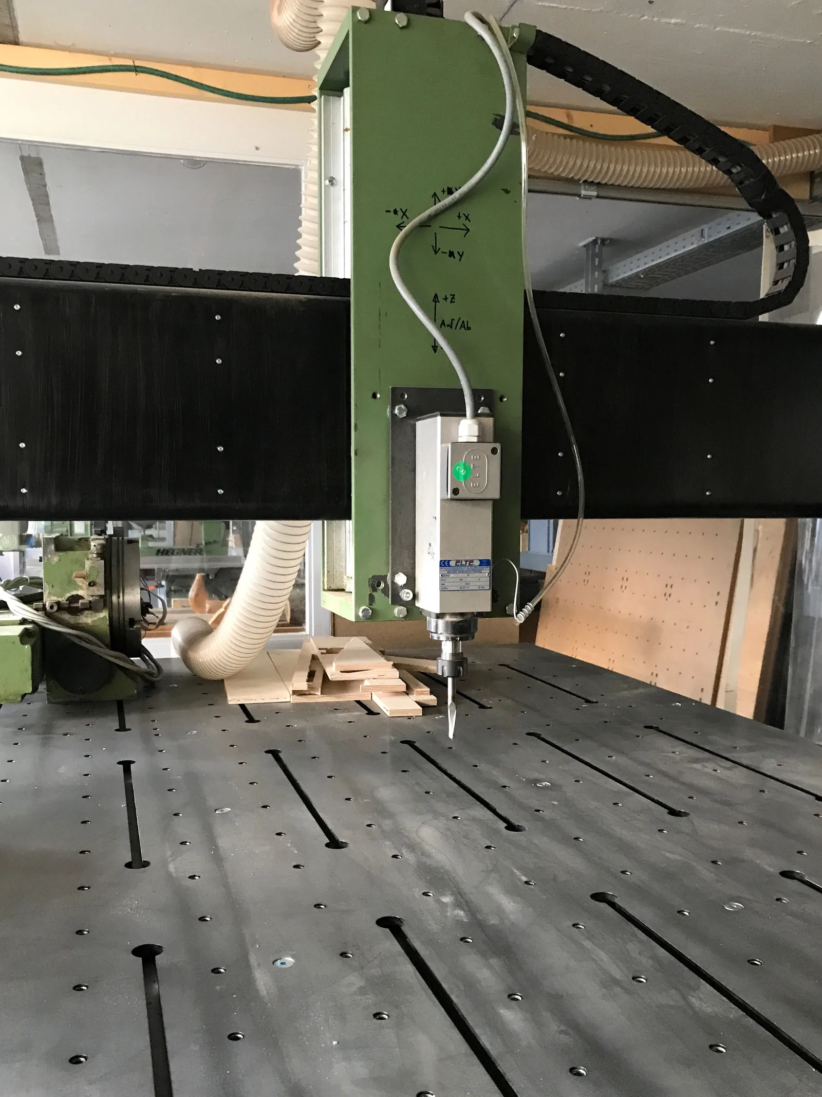 Grüne Frässpindel der CNC-Portalfräse über dem Nutentisch, daneben der Absaugschlauch