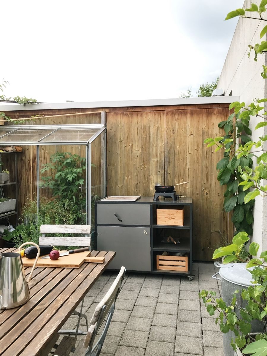 Aussenküche im Garten vor einer Holzwand, daneben ein gedeckter Tisch