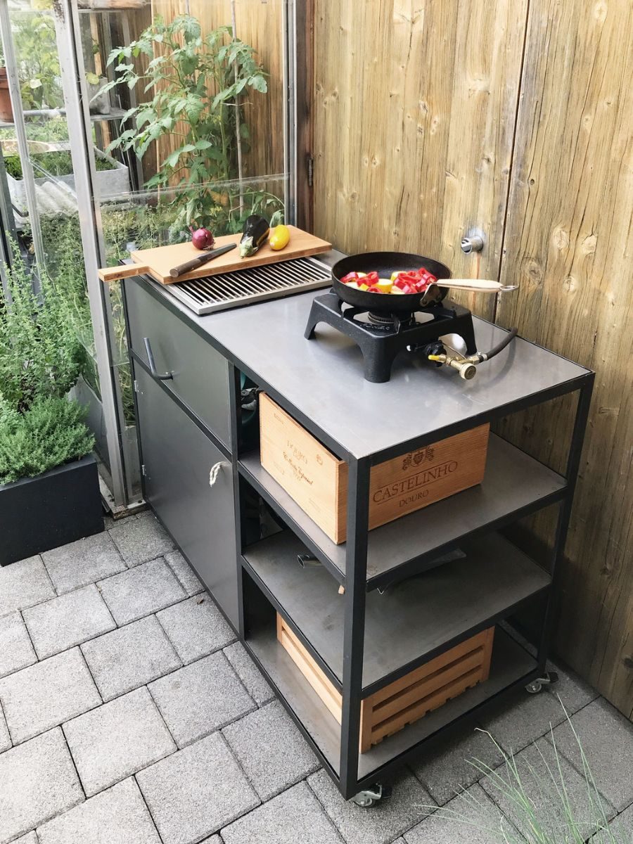 Fahrbare Aussenküche aus Stahl mit Arbeitsfläche, Gaskocher und Holzkisten als Ablage, auf einer Terrasse